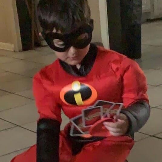 Boy dressed as a superhero holding uno cards